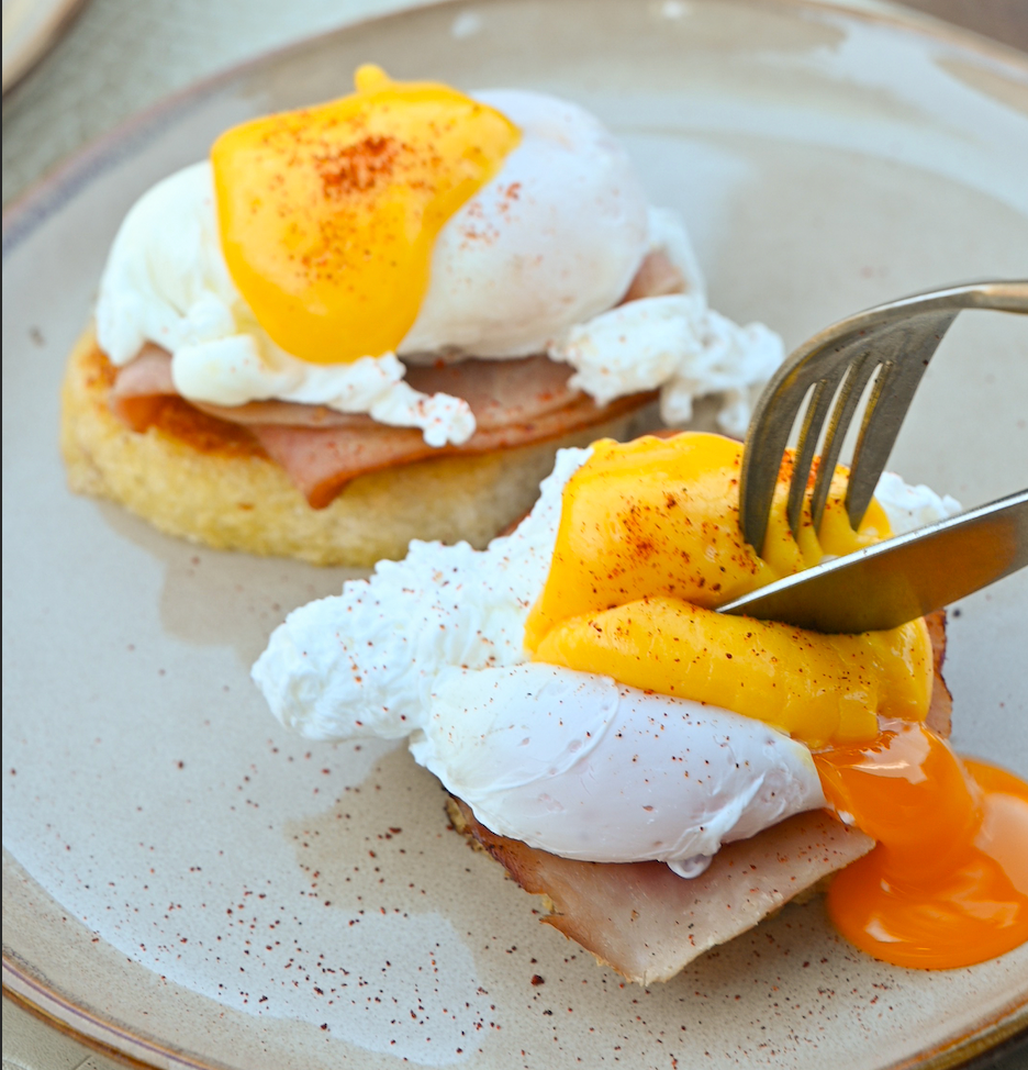 Two servings of eggs benedict on a speckled plate with a fork and knife.
