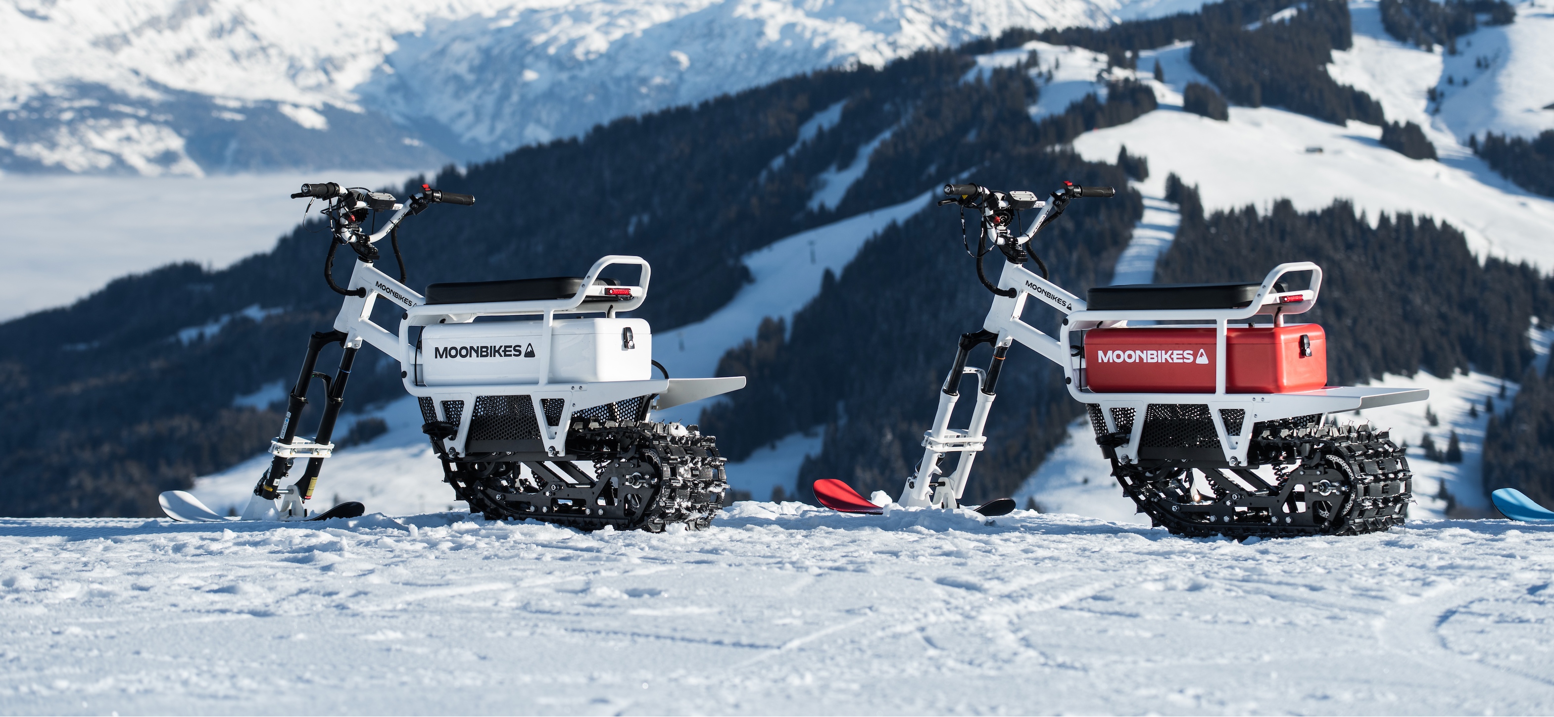 Two snowmobiles on a snowy landscape with mountains in the background
